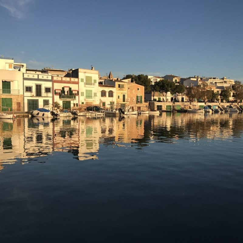 Hafen von Porto Colom auf Mallorca mit traditionellen Fischerhäusern und Bootsgaragen am Wasser